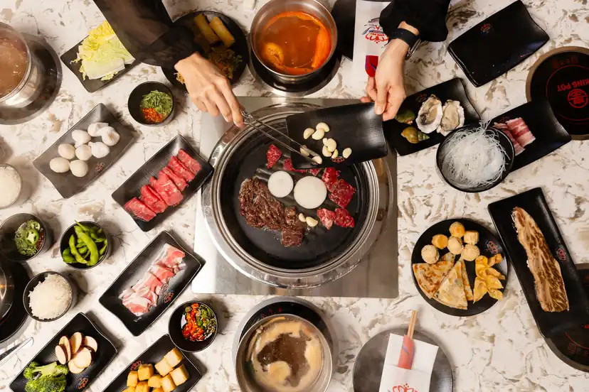 Overhead view of a King Pot table with a tabletop grill, hotpots and plates of meat